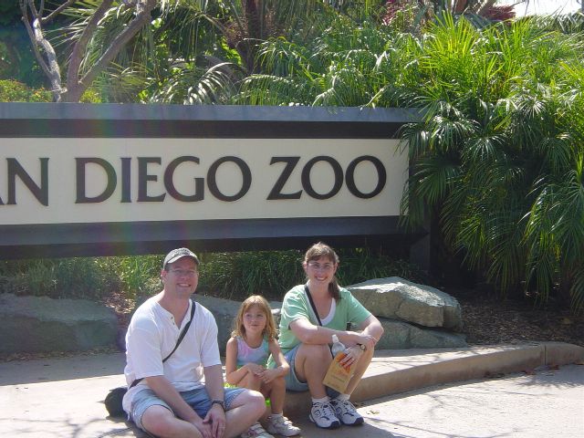 James, Julie, and Isabella sitting in front of a sign reading San Diego Zoo