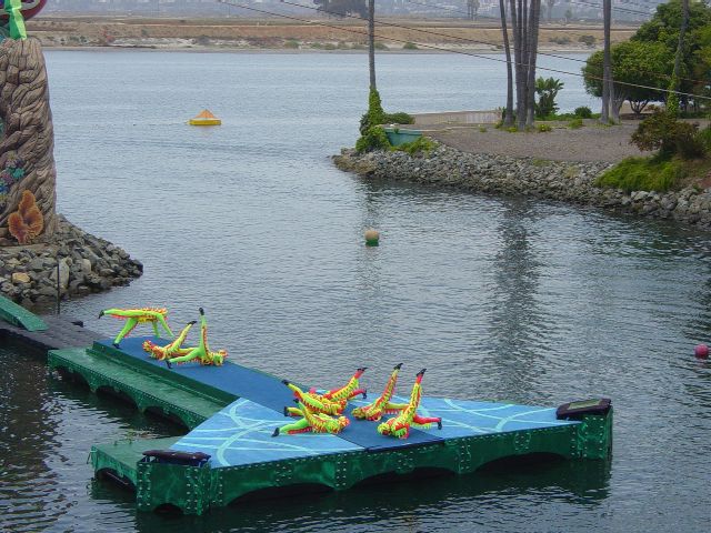 Acrobats in bright yellow and pink costmes perform on a stage over water