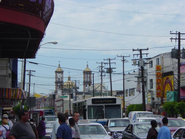 Cars and busses under power lines in front of a cathedral with gold tile roofs