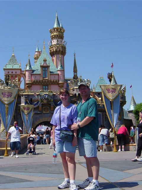 James and Julie in front of a pink and blue castle with gold highlights