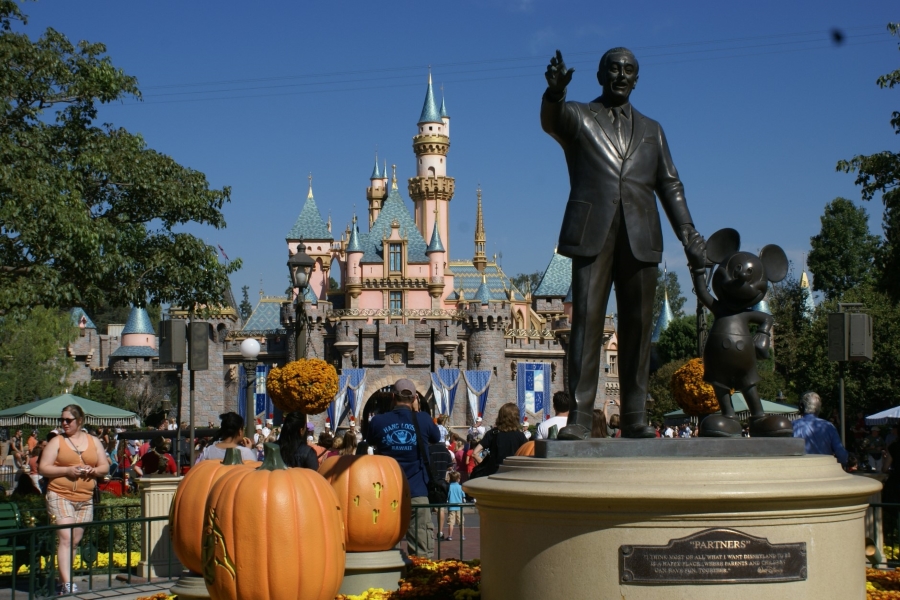 A statue of Walt Disney holding Mickey Mouse’s hand stands in front of Sleeping Beauty’s Castle