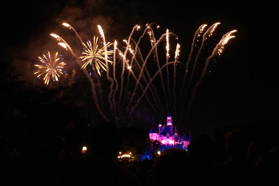 Gold fireworks explode in the skies over a castle lit with pink lights