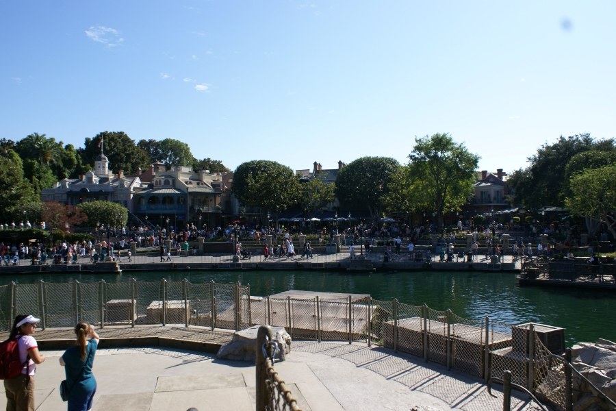 Julie and friend on a large wooden landing look across a lagoon at the people waiting to go on rides