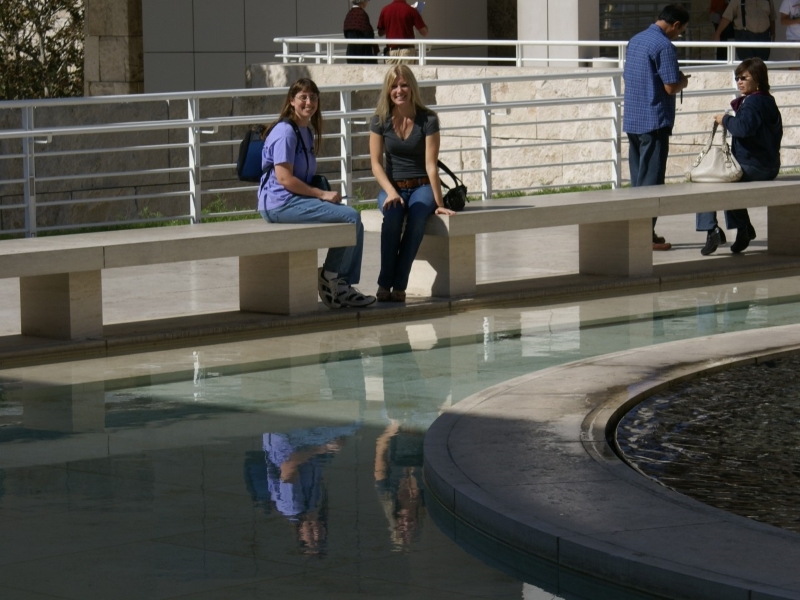Julie and her sister sit on a bench with their reflections visible in a pool of calm water