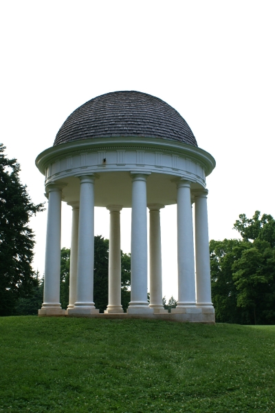 A shingled dome supported by nine tall white columns stands atop a hill surrounded by trees