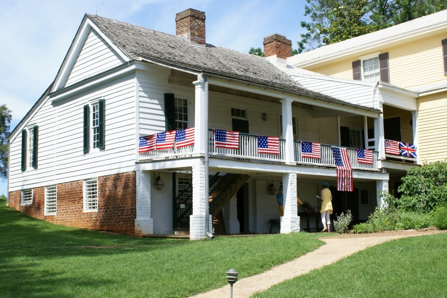 A white siding clad house extends out of the side of a hill creating a walkout lower level with American flags draped on the railing