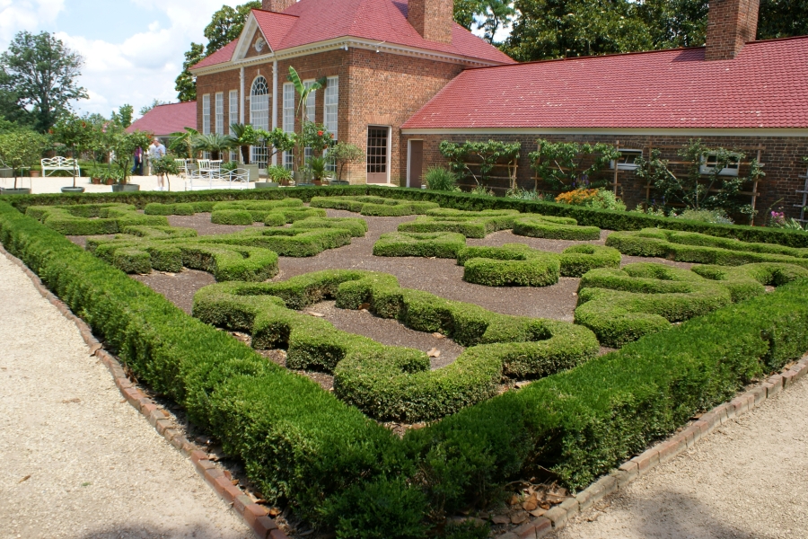 Carefully groomed hedges form a pattern in a formal garden behind a brick clad structure