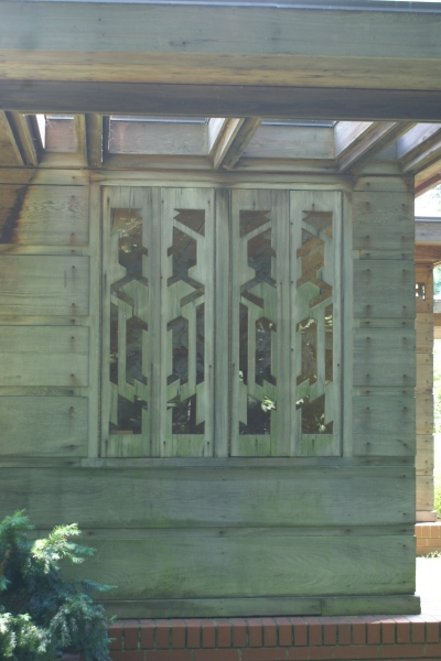 Intricately cut wood panels act as shutters for a window in a faded wood paneled wall