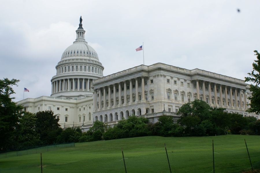 The American Flag stands on the corner of large white multi-story building with an expansive central dome towering above the rest of the structure