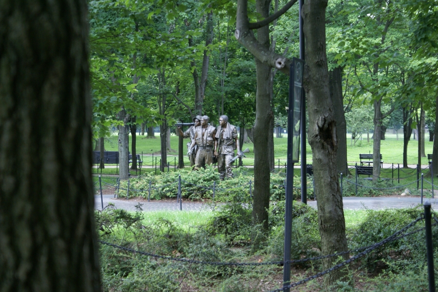Patinaed statues of men in army combat gear stand amongst trees