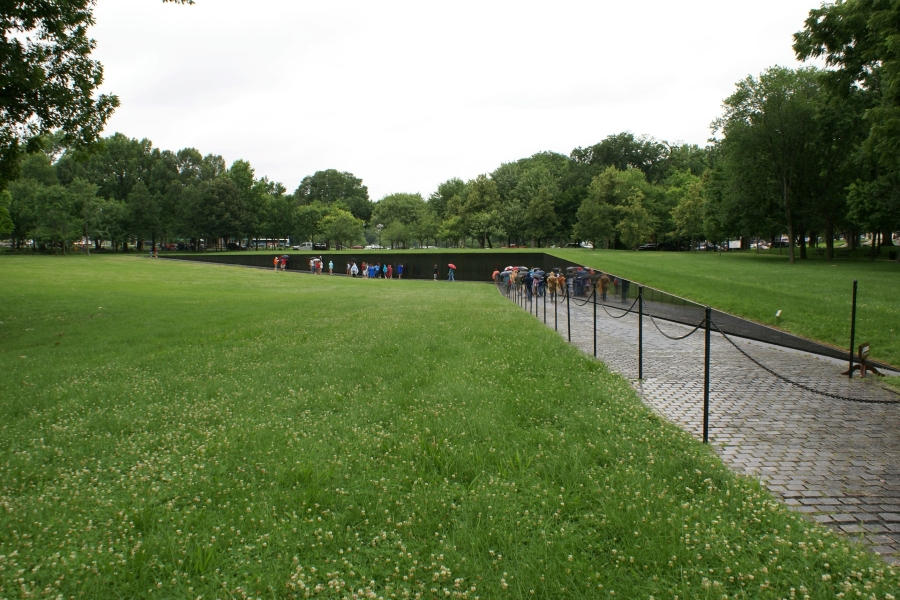 Grass slopes down a hill with a walk along a black “V” retaining wall with names etched in the surface