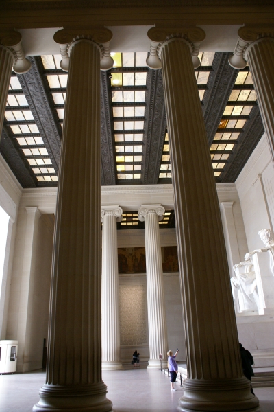 The stark white statue of a man sitting in a large solid chair is visible between tall columns