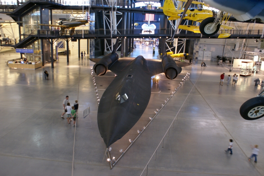 A sleek black airplane shaped roughly like a “V” sits on a polished concrete floor