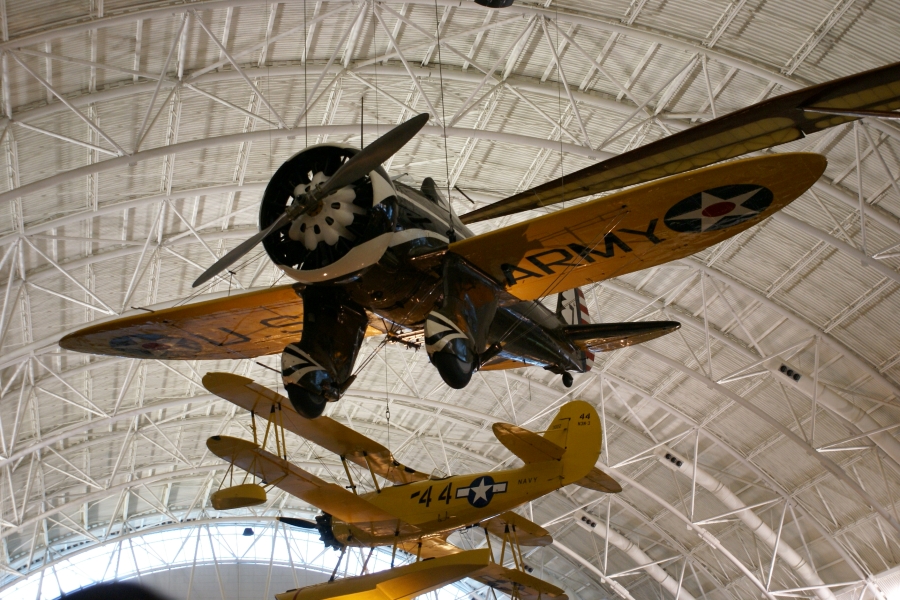 Several different style airplanes hang from the ceiling of a large hanger