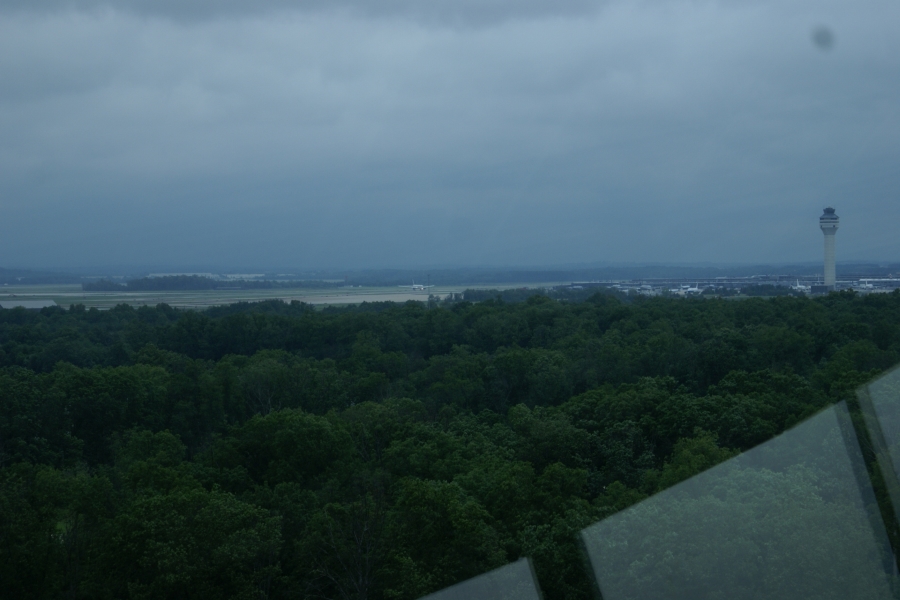 Trees give way to a runway with a plane taking off as seen from a high vantage point