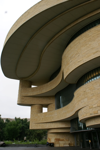 Curved planes of yellowish stone and brick extend over a pool 3 stories below
