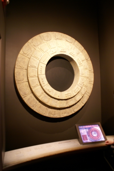 Three concentric tan stone rings with various symbols hang on a wall