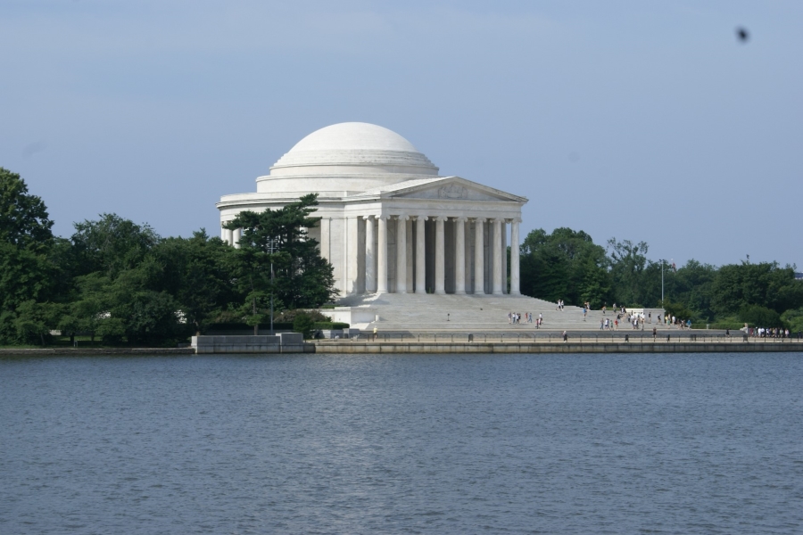 A bright white domed monument with tall columns stands amongst the trees beyond a body of water