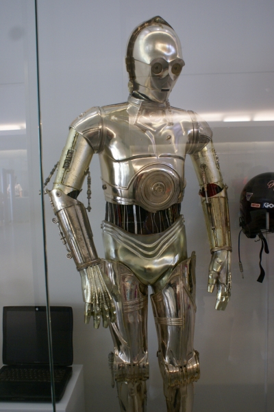A silvery metallic humanoid form with exposed wiring across the midriff on display in a large case