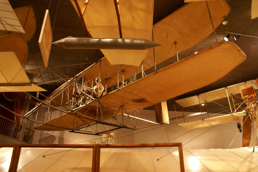A full size wooden model of a bi-wing aircraft with fabric wings hangs from the ceiling