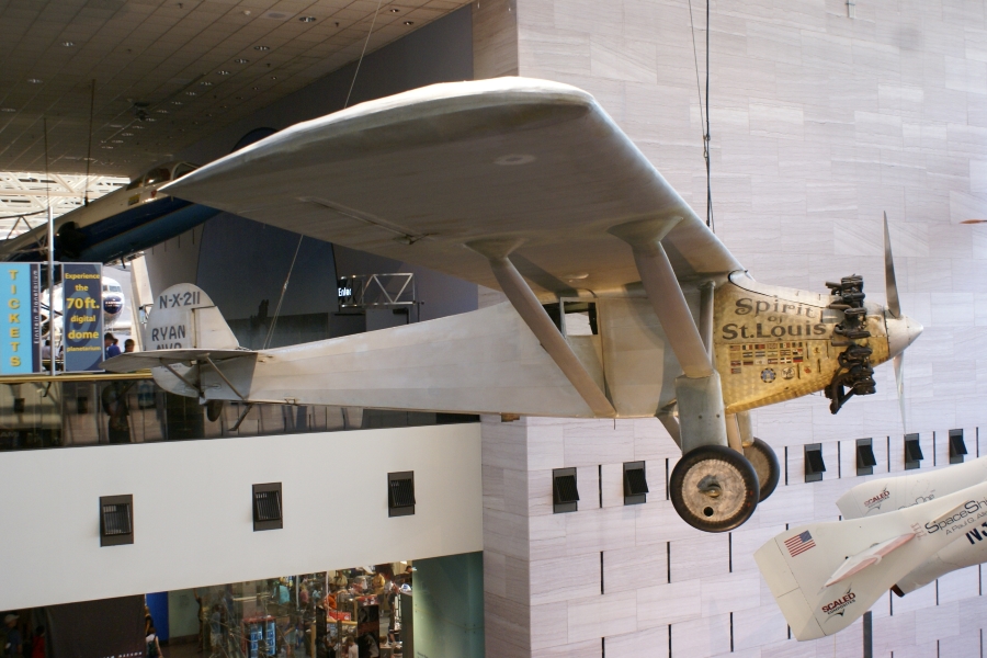 A white airplane with gold engine housing and wooden prop hangs in the air