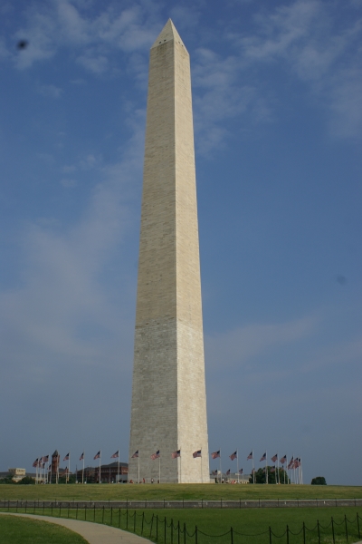 A white obelisk encircled by US flags extends up from a grassy hill