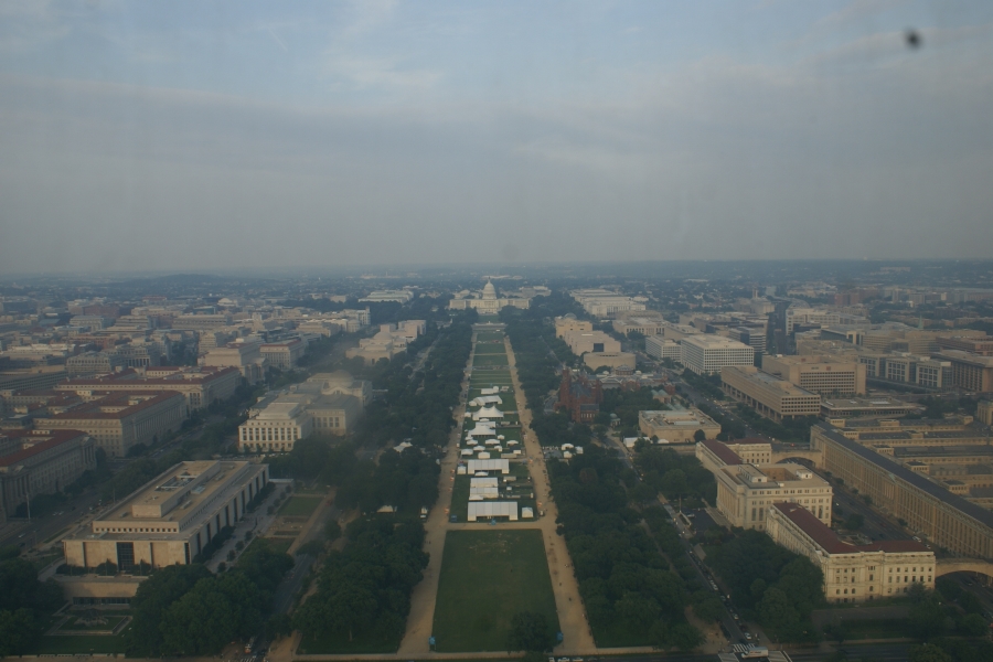 A green park area extends between buildings before ending before a large white building with a cupola and dome at the center