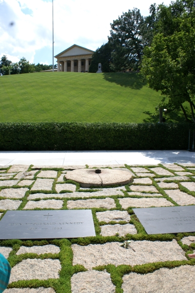 A small black disk with a flame above sits in a field of rough stone pavers with flat grave makers nearby