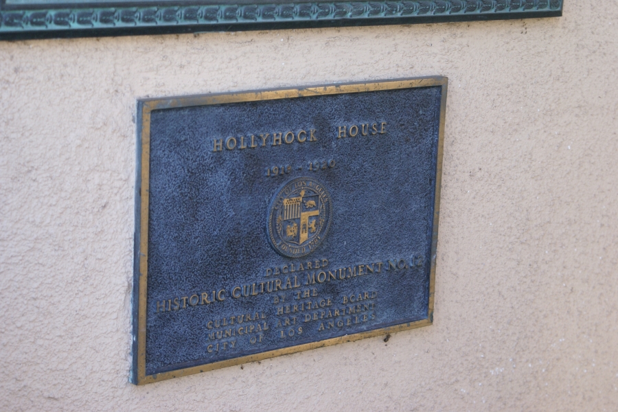 A bronze plaque embedded in a tan stucco wall identifies Hollyhock House as Historic Cultural Monument in the City of Los Angeles