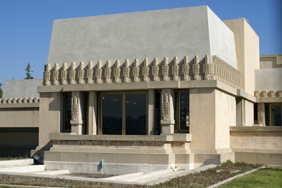 Tan stucco blocks surround windows with a repetitive detail with six small squares to each side of a center taller stalk appears between the glazing and marching across the header