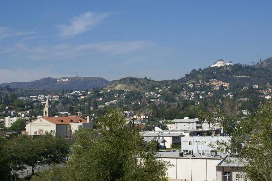 A stark white building sits on top of a hill with houses running down the slopes below while white letters stand out on another hill to the left