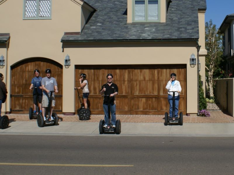 Six people on segways in front of a garage across the street from the photographer