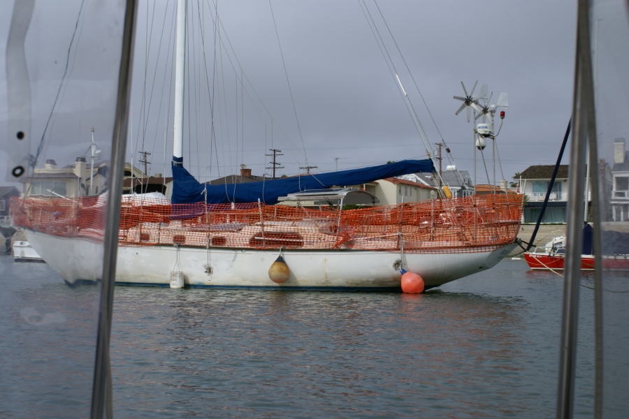 Bright orange plastic mesh fencing wraps around the deck rail of a white hulled sailing ship