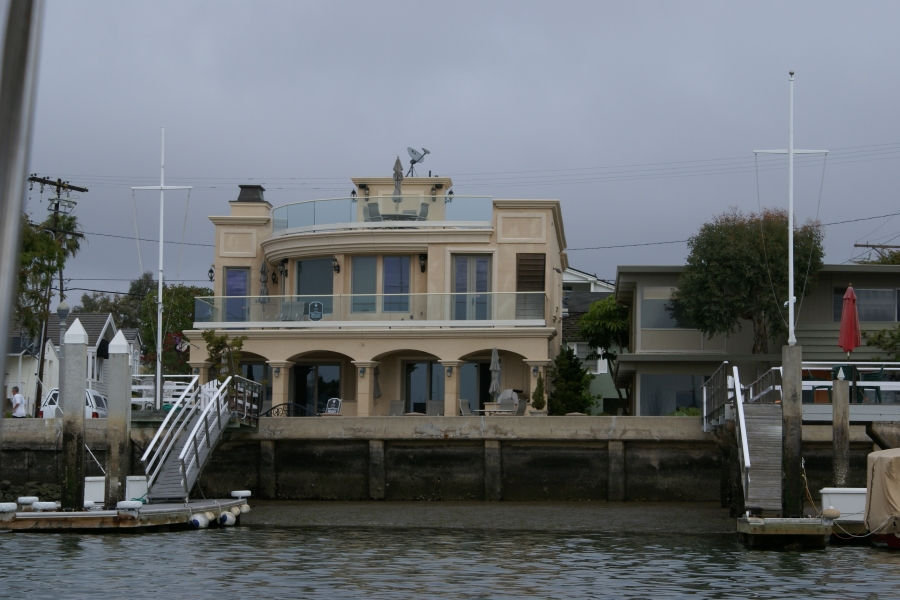 A Mediterranean style villa with glass railings sits on top of a sea wall with a ramp to a floating dock