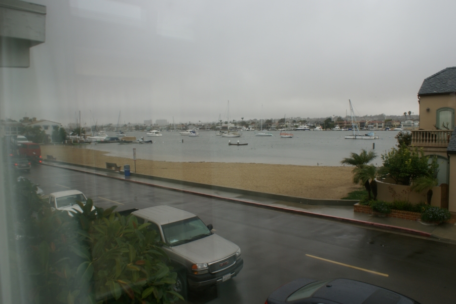 gray clouds hang over wet streets and a small stretch of sand with sailboats anchored in the water beyond
