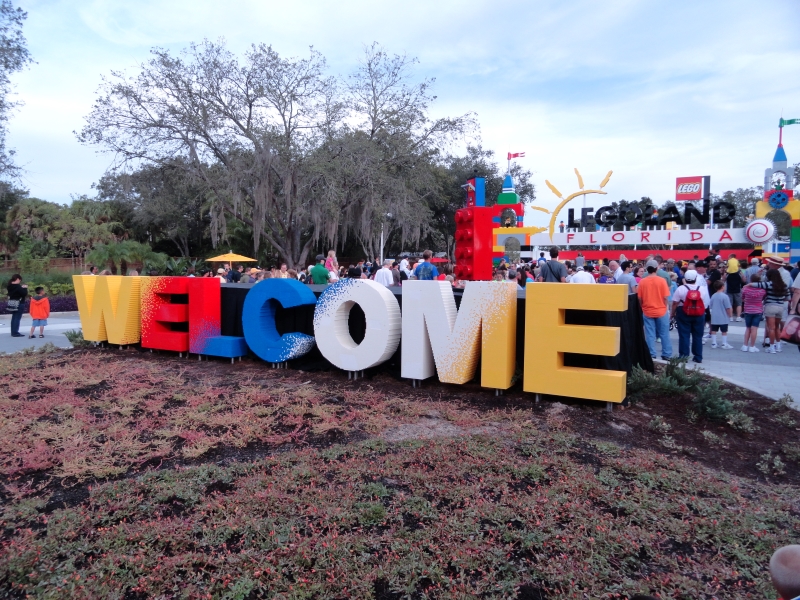 Two-foot-tall letters spelling “welcome” are made of multi-colored LEGO bricks and sitting on a grassy island surrounded by sidewalks