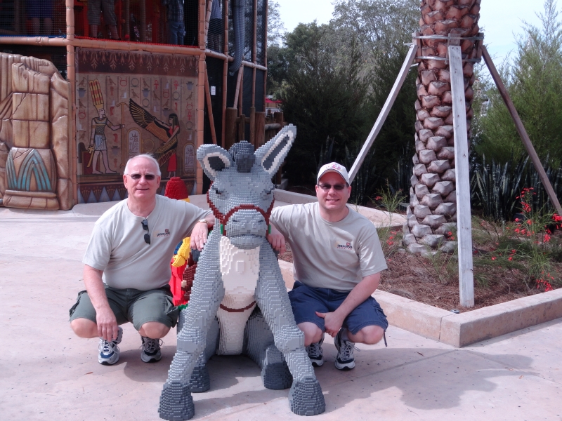 Jim and James squat next to a life size LEGO model of a burro