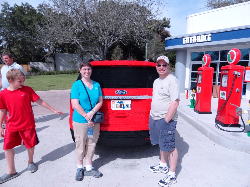 James and Julie stand at then read bumper of a full-size model of a red Ford Explorer made from LEGO