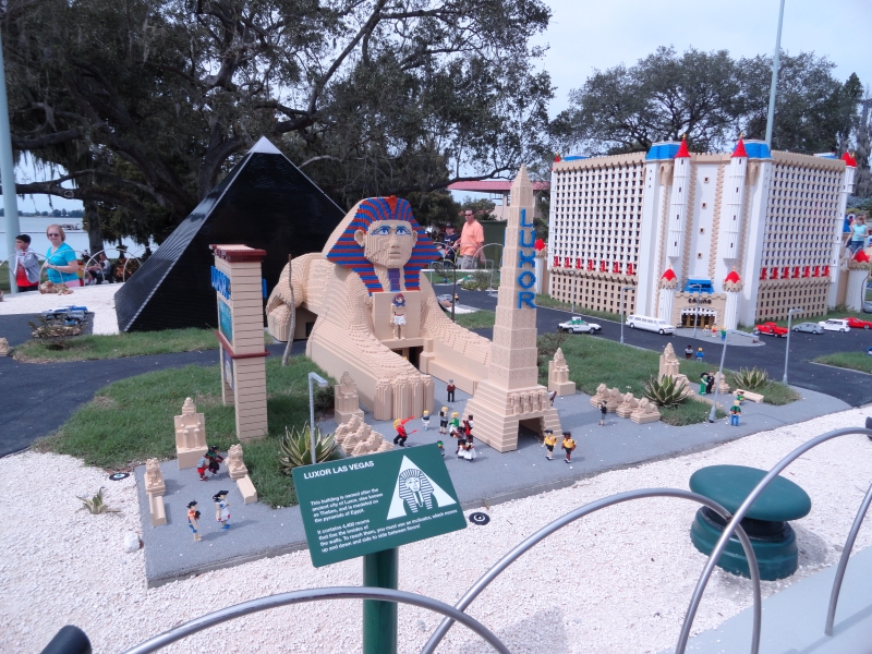 People walk around looking at large LEGO models of a sphinx, black pyramid, and large white building with a castle like roof line in a diorama dedicated to building in Las Vegas