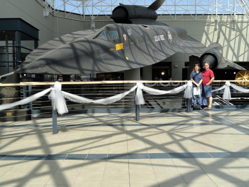 James and Julie stand near a railing with a black US Air Force plane suspended behind them
