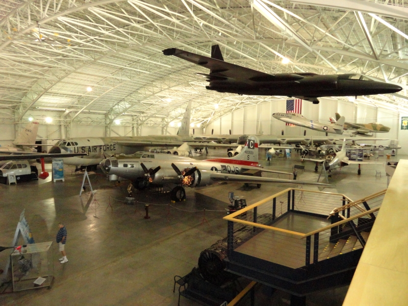 A black plane with long wings hangs from an arched ceiling of a hanger with several large planes on display inside