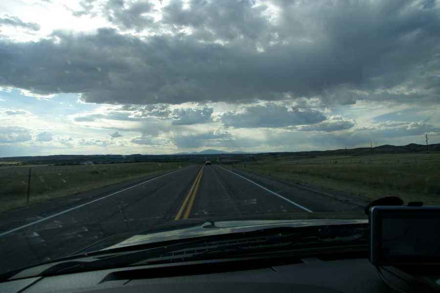 Clouds in the sky cast shadows on the road with mountains extending above the horizon