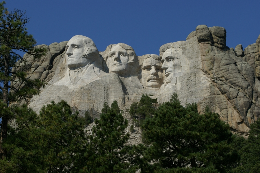 Four bright white faces look out from large stone walls above tall fir trees