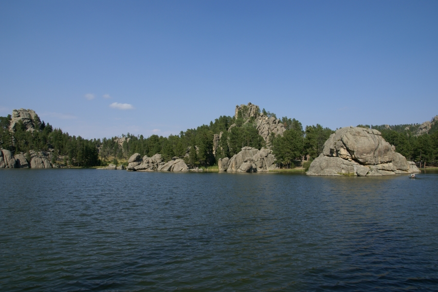 Deep blue waters reflect the clear sky and fir tree covered slopes of the stone hills surrounding a lake