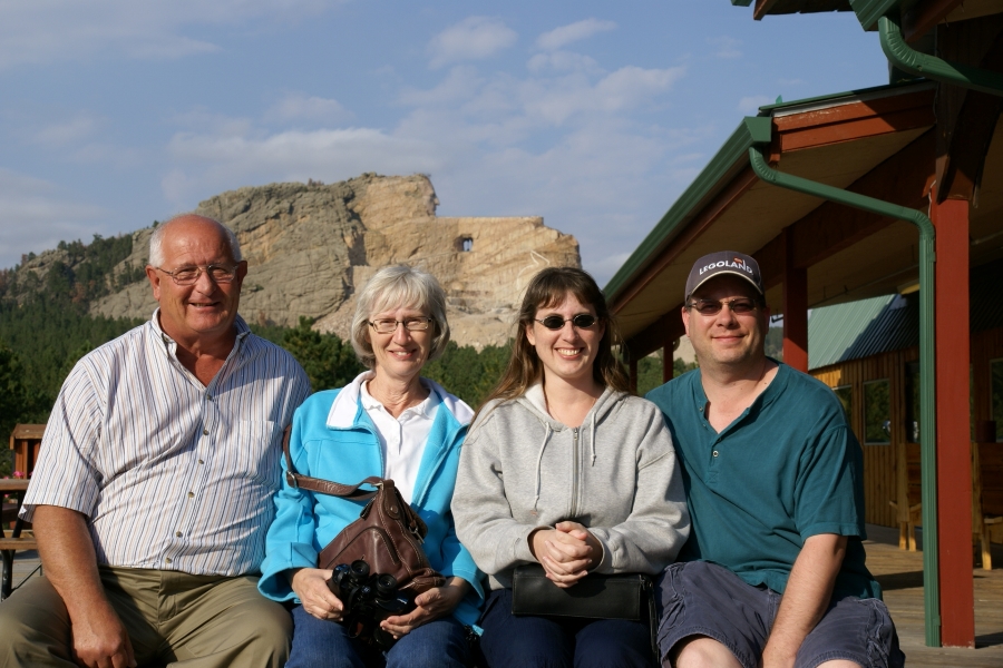 Gary, Surella, Julie, and James sit near a cedar wood building with the Crazy Horse Mountain Memorial in the distance