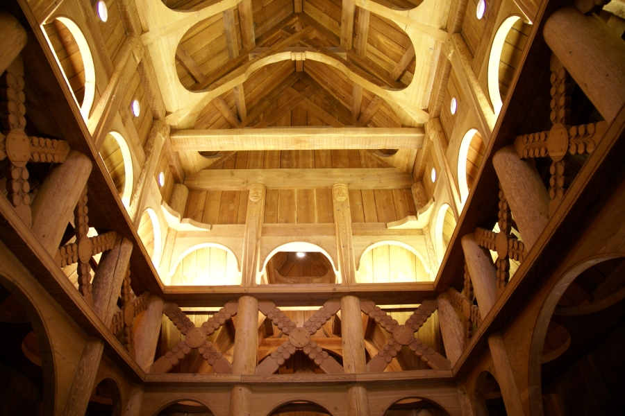 Curved wooden arches and carved braced accents support the high ceiling in the center of a the all wood stave church