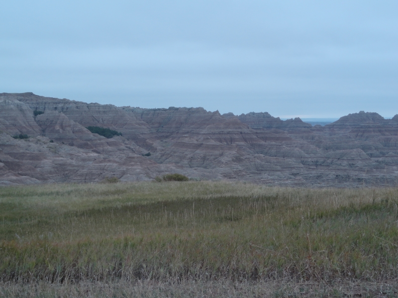 Low scrub grass gives way to stone hills with various color stripes below a cloudy sky