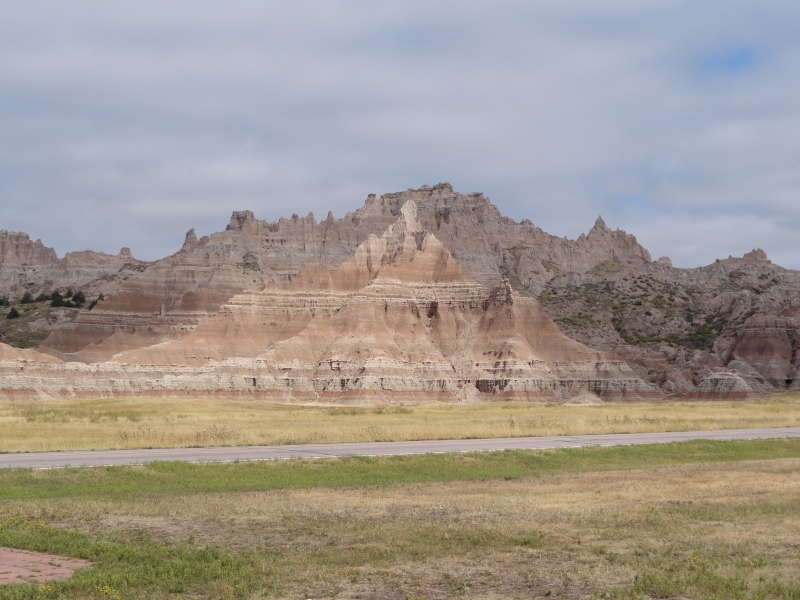 Sun breaks through the clouds highlighting a small portion of the layered rock showing colors of many colors of tan and light red in the rocks of the badlands