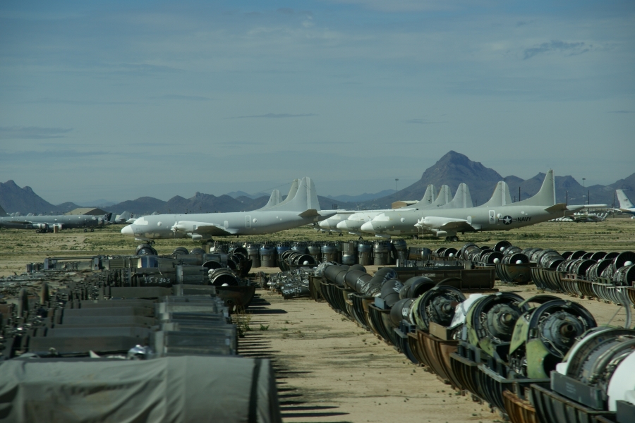 Large turbine jet engines sit in storage bins in front of a line of Navy transport planes