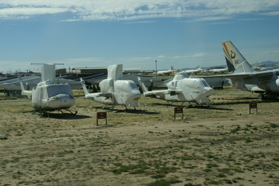 Three different styles of helicopters sit near the drive lane with the white coating over their windows